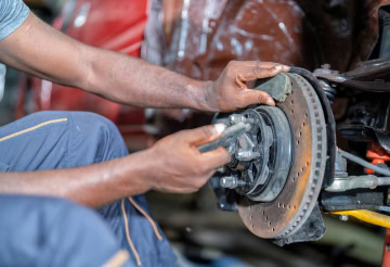 Mechanic inspecting car brake disc during maintenance at auto shop.