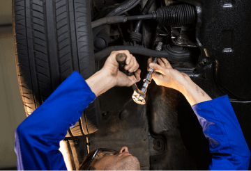 Auto mechanic inspecting vehicle undercarriage for maintenance.