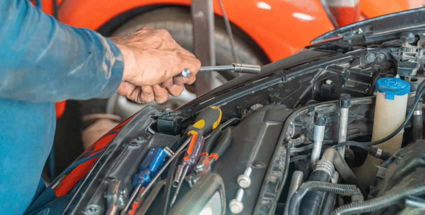 Technician inspecting car engine for transmission issues at auto repair shop.