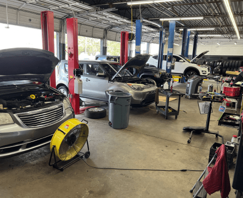 Auto repair shop with several cars being serviced, including open hoods, repair tools, and equipment.