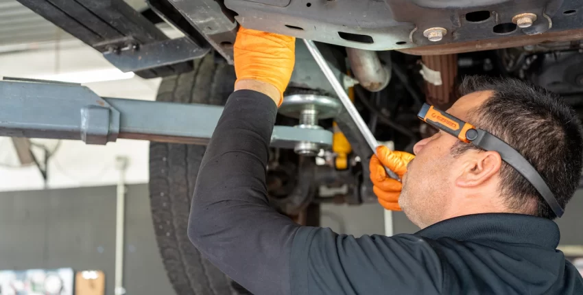 Engine repair technician inspecting undercarriage of vehicle in auto repair shop.