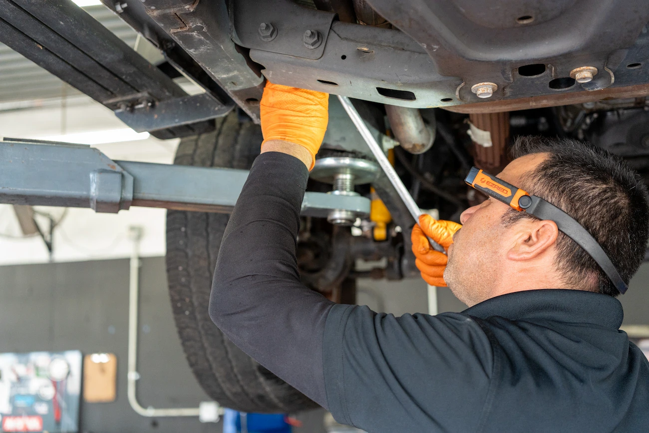 Engine repair technician inspecting undercarriage of vehicle in auto repair shop.