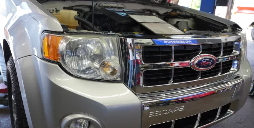 Close-up of Ford Escape engine with hood open at auto repair shop.