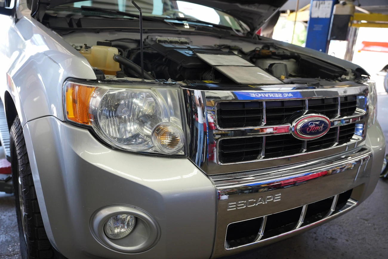 Close-up of Ford Escape engine with hood open at auto repair shop.