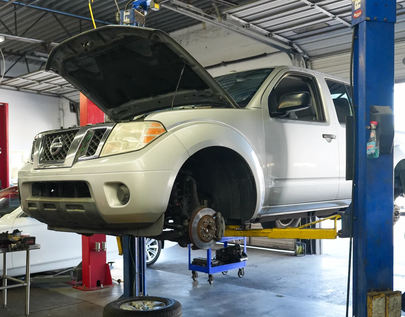 Silver Nissan Frontier on lift with open hood at Orlando auto repair shop.