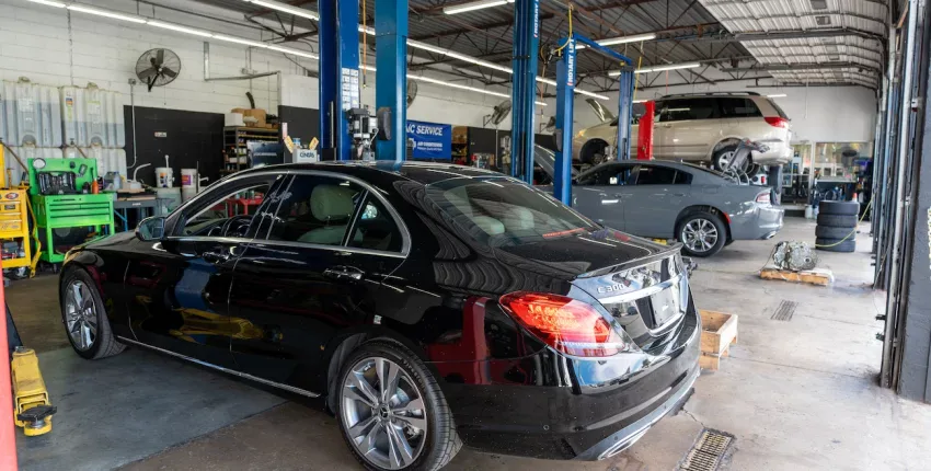 Black luxury sedan inside Orlando auto repair shop with vehicle lifts and tools.