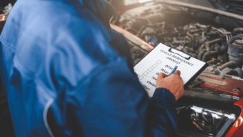 Diesel engine technician inspecting performance checklist under the hood.