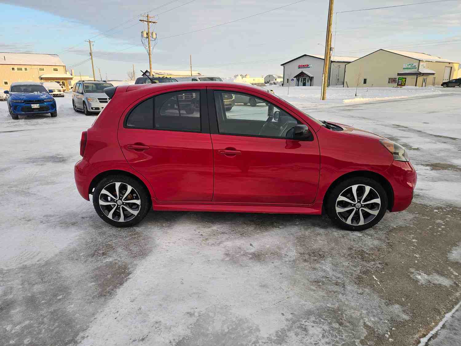 Red compact car parked on snowy lot in Pembina Valley, Manitoba.