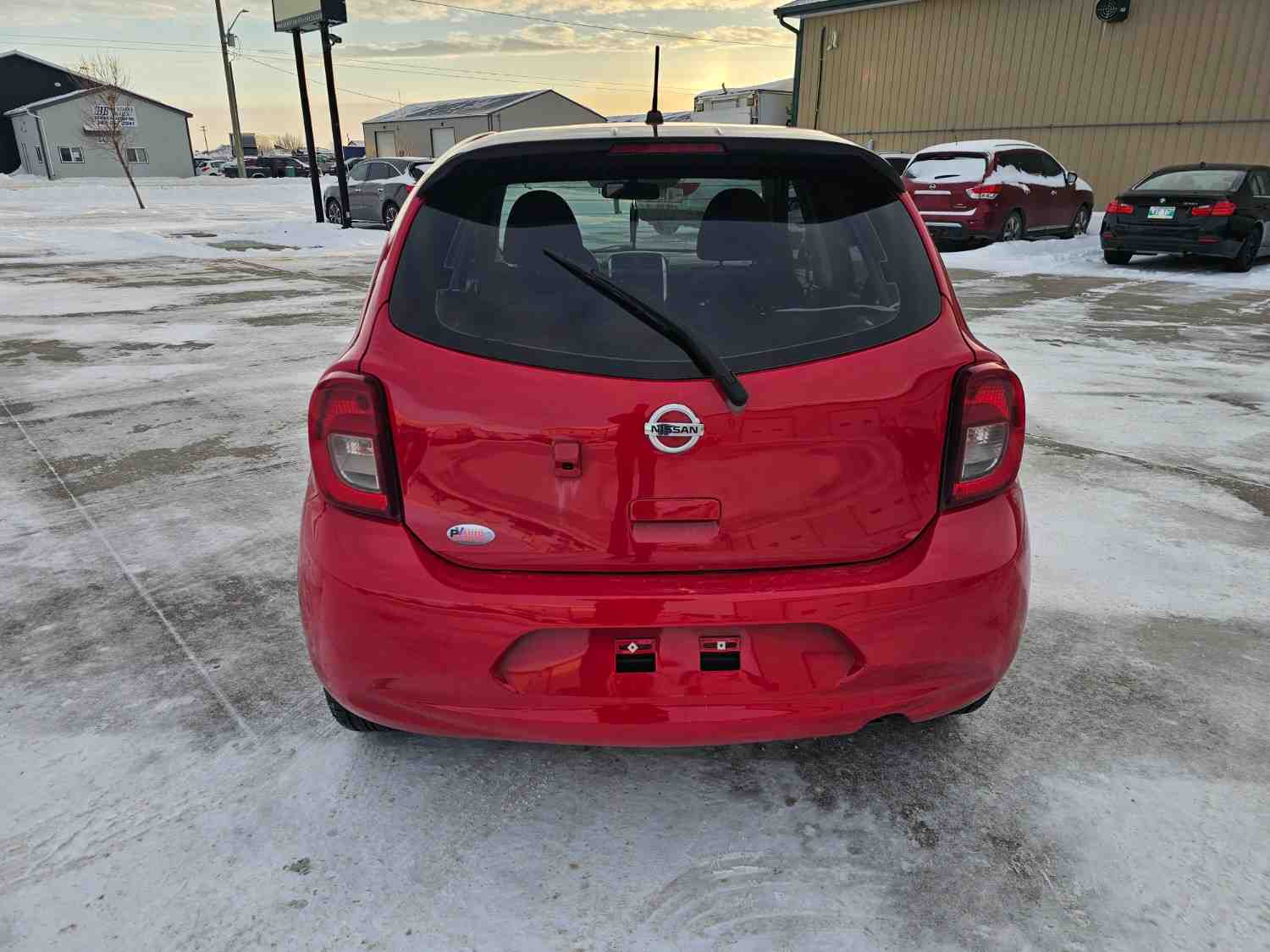 Red Nissan Micra parked in Pembina Valley lot with snow and industrial buildings.