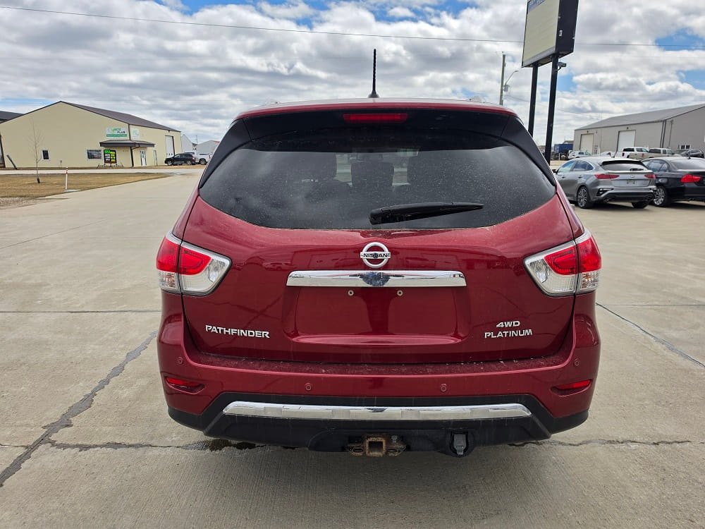 Red Nissan Pathfinder SUV in dealership lot, rear view, outdoors.