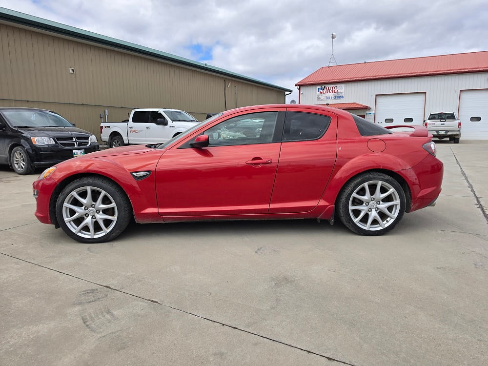 Red Mazda RX-8 sports car parked outside Pembina Valley Auto dealership.