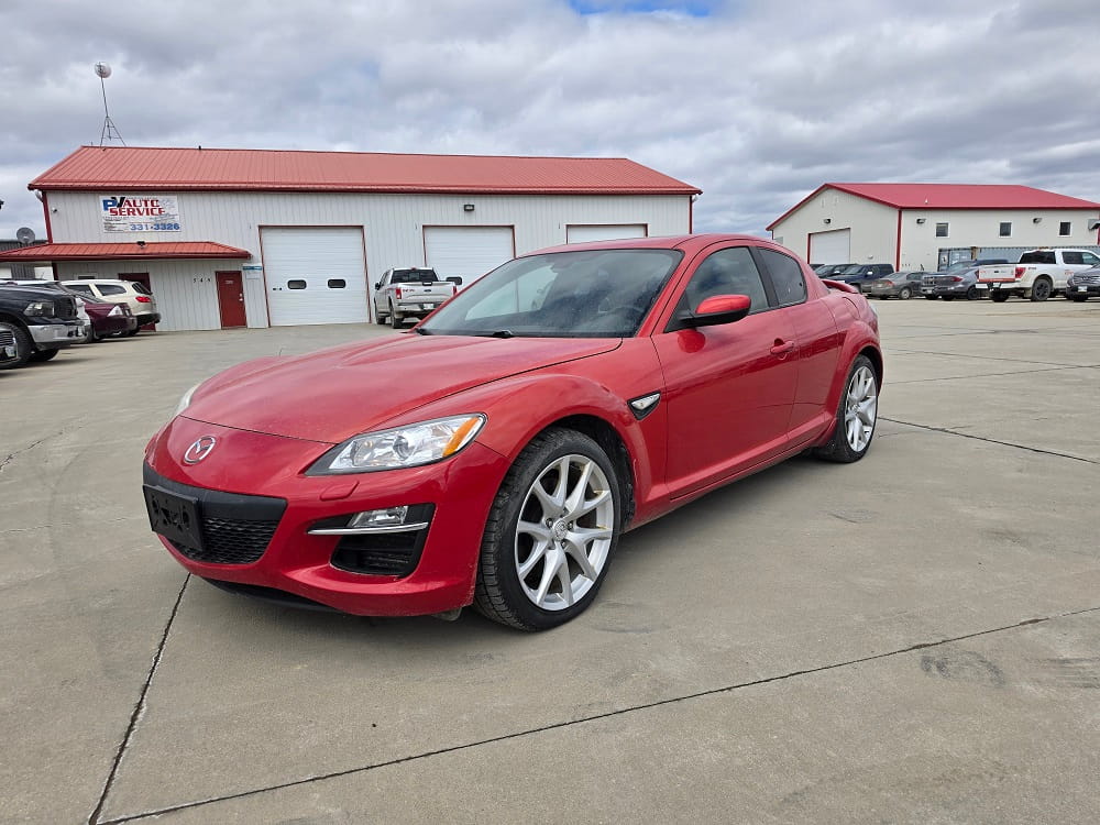 Red Mazda RX-8 sports car parked in front of Pembina Valley Auto dealership.