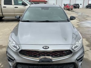 Silver Kia Forte parked outside Pembina Valley Auto dealership on a cloudy day.