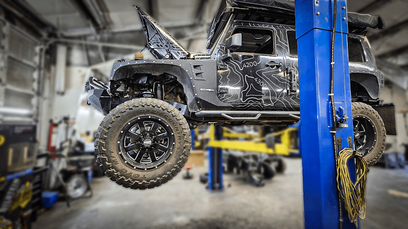 Off-road vehicle lifted on hydraulic lift at Performance Authority, showcasing custom modifications.