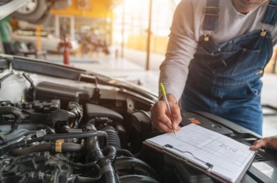 Professional mechanic inspecting car engine and taking notes at Performance Authority.