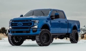 Blue Ford pickup truck with rugged tires in snowy landscape.