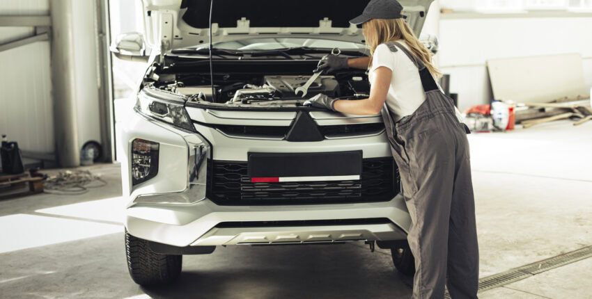 Woman inspecting car engine at Performance Authority auto repair shop.