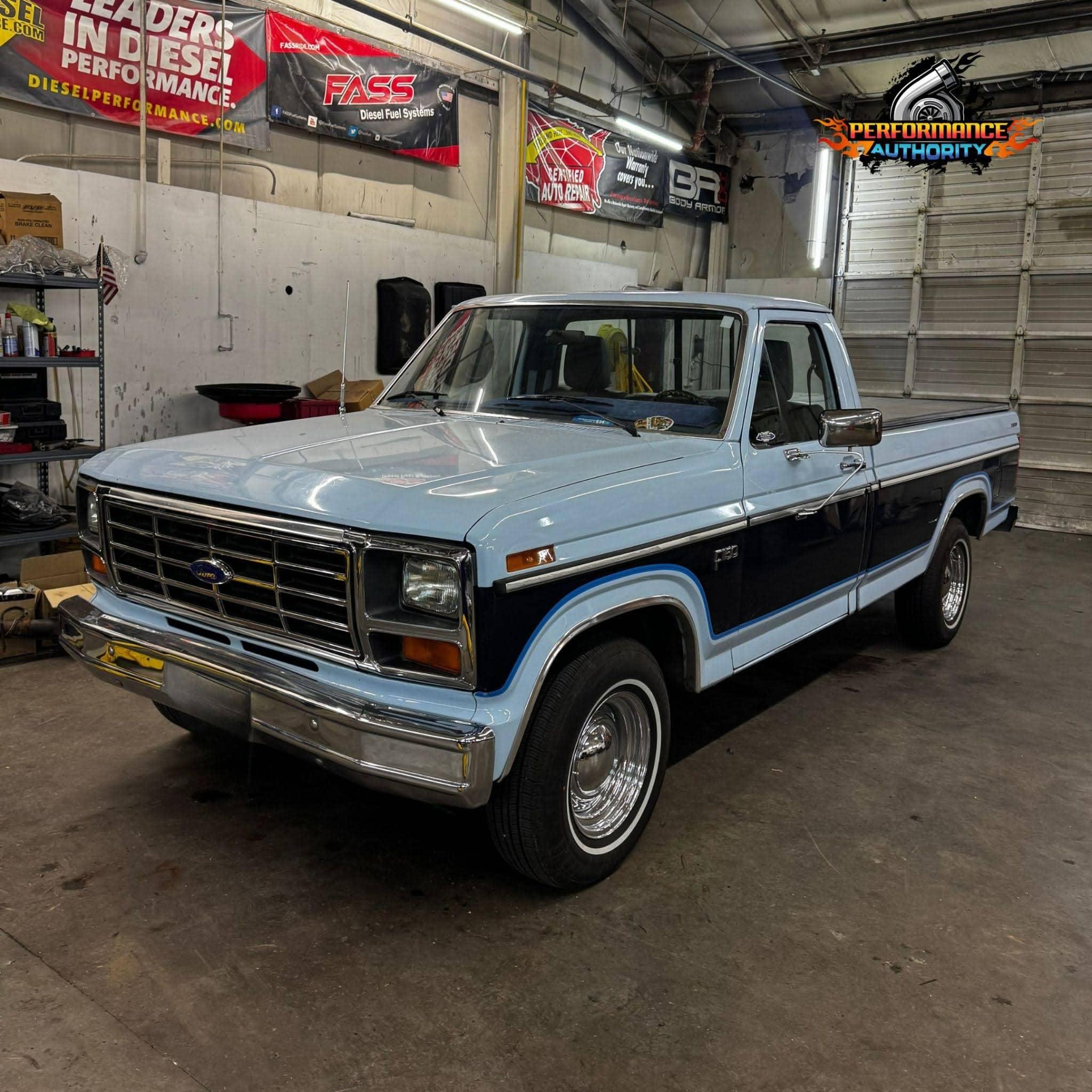 Vintage blue and black Ford pickup truck inside Performance Authority workshop.