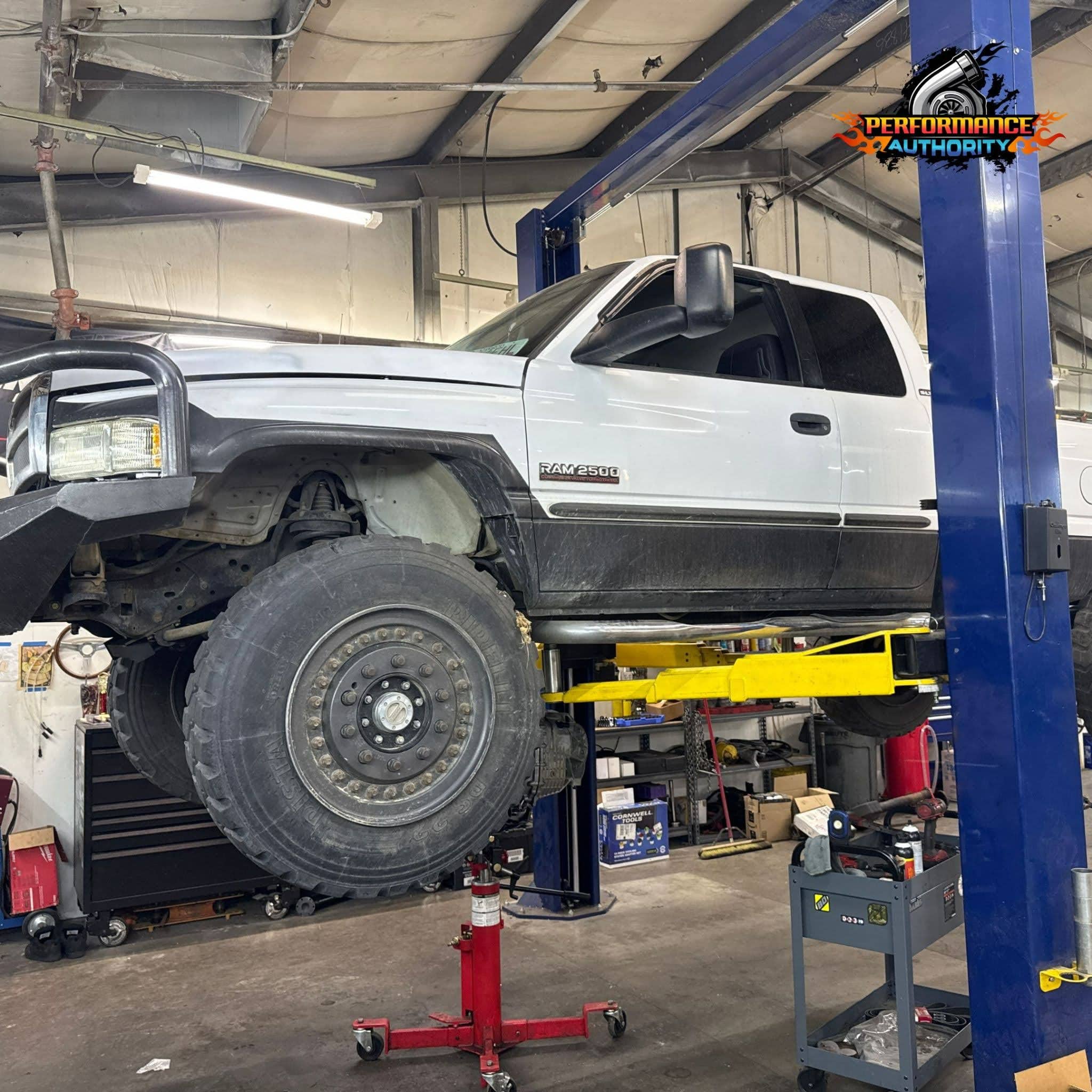 White pickup truck on hydraulic lift at Performance Authority auto shop.