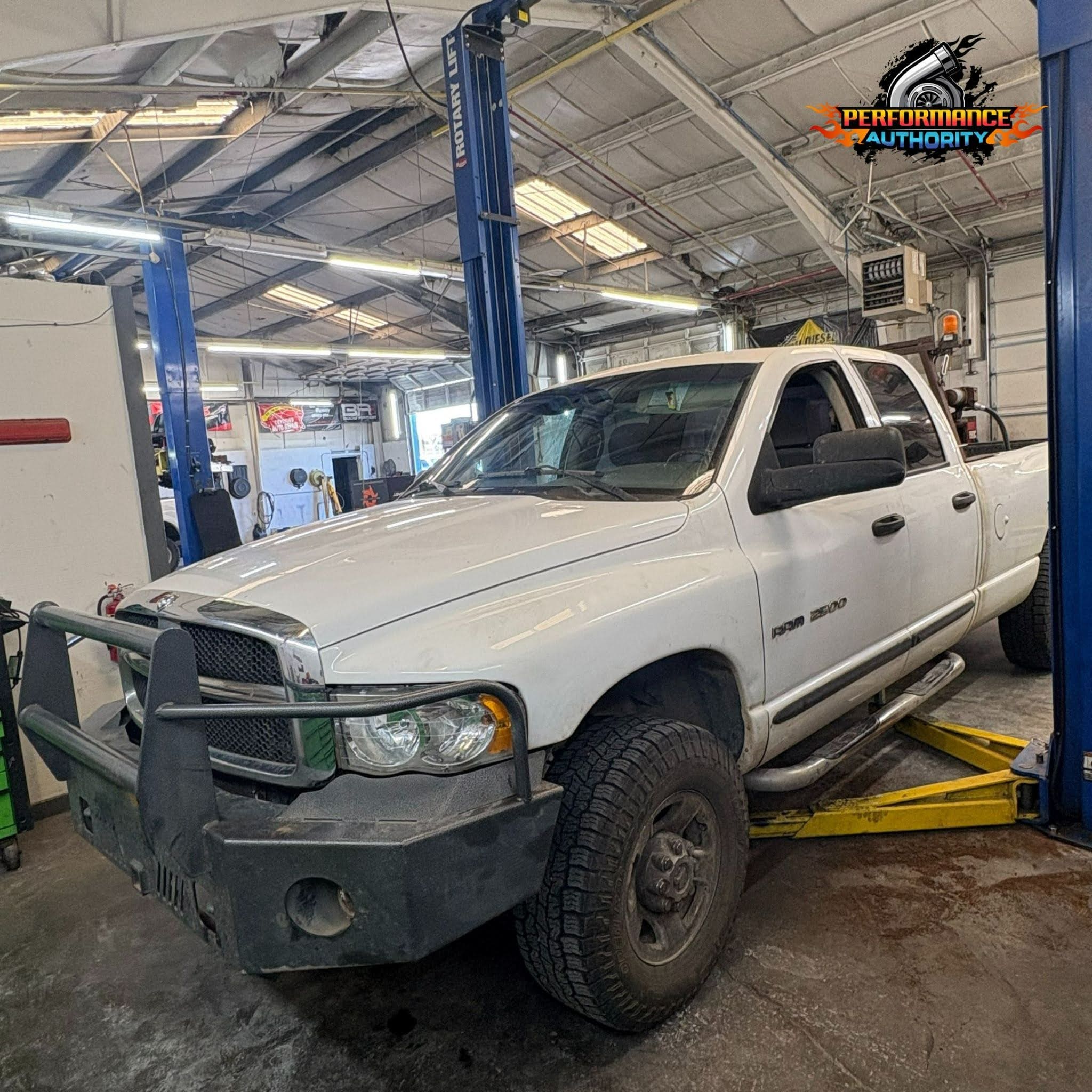 White Dodge Ram truck in repair shop with lift and tools.