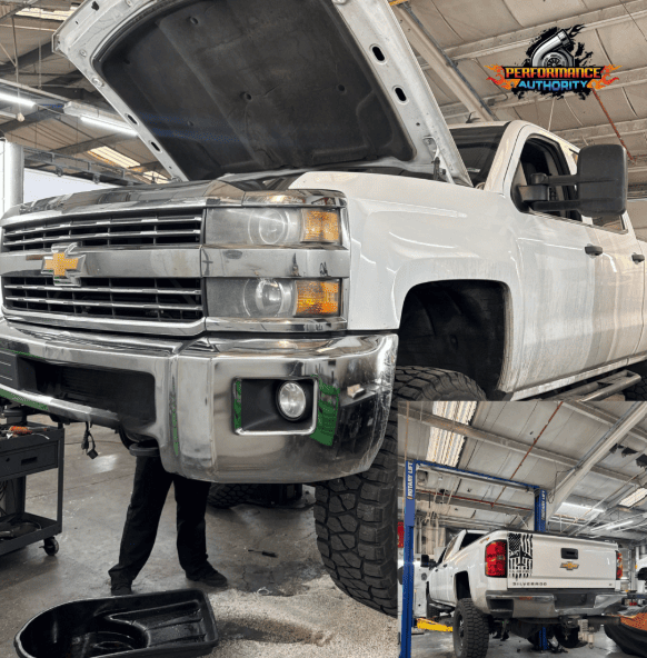 White Chevrolet truck lifted in a garage with open hood, undergoing repair at Performance Authority.