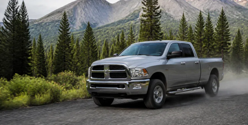 Silver pickup truck driving on mountain road surrounded by pine trees and mountains.