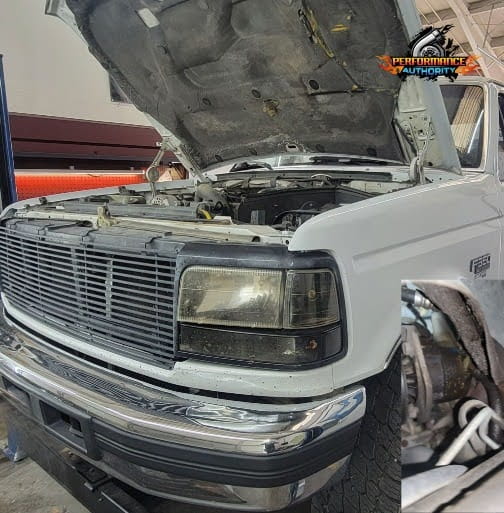 White truck with open hood at Performance Authority repair shop.