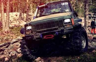 Off-road Jeep vehicle driving over rocky trail in forested area.