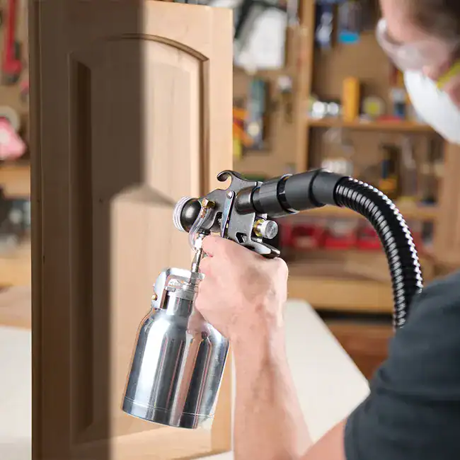 Person spray painting wooden cabinet