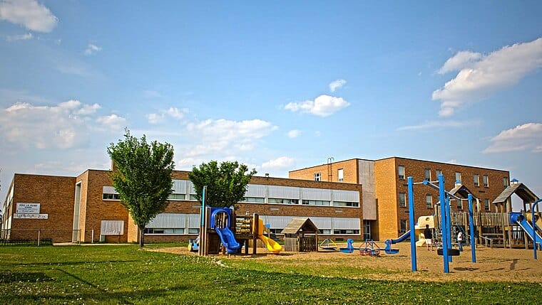 Brightly painted playground equipment at a school or community center with colorful slides and climbing structures, set against a modern brick building and clear blue sky.
