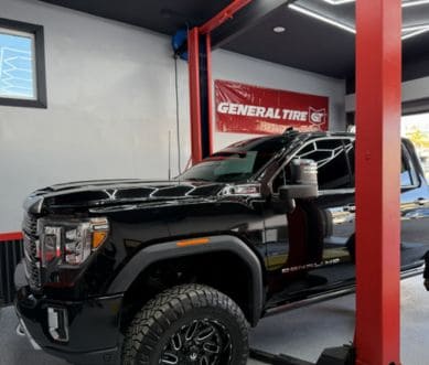 Auto repair shop with a black truck on a lift, specializing in tire and vehicle maintenance services.