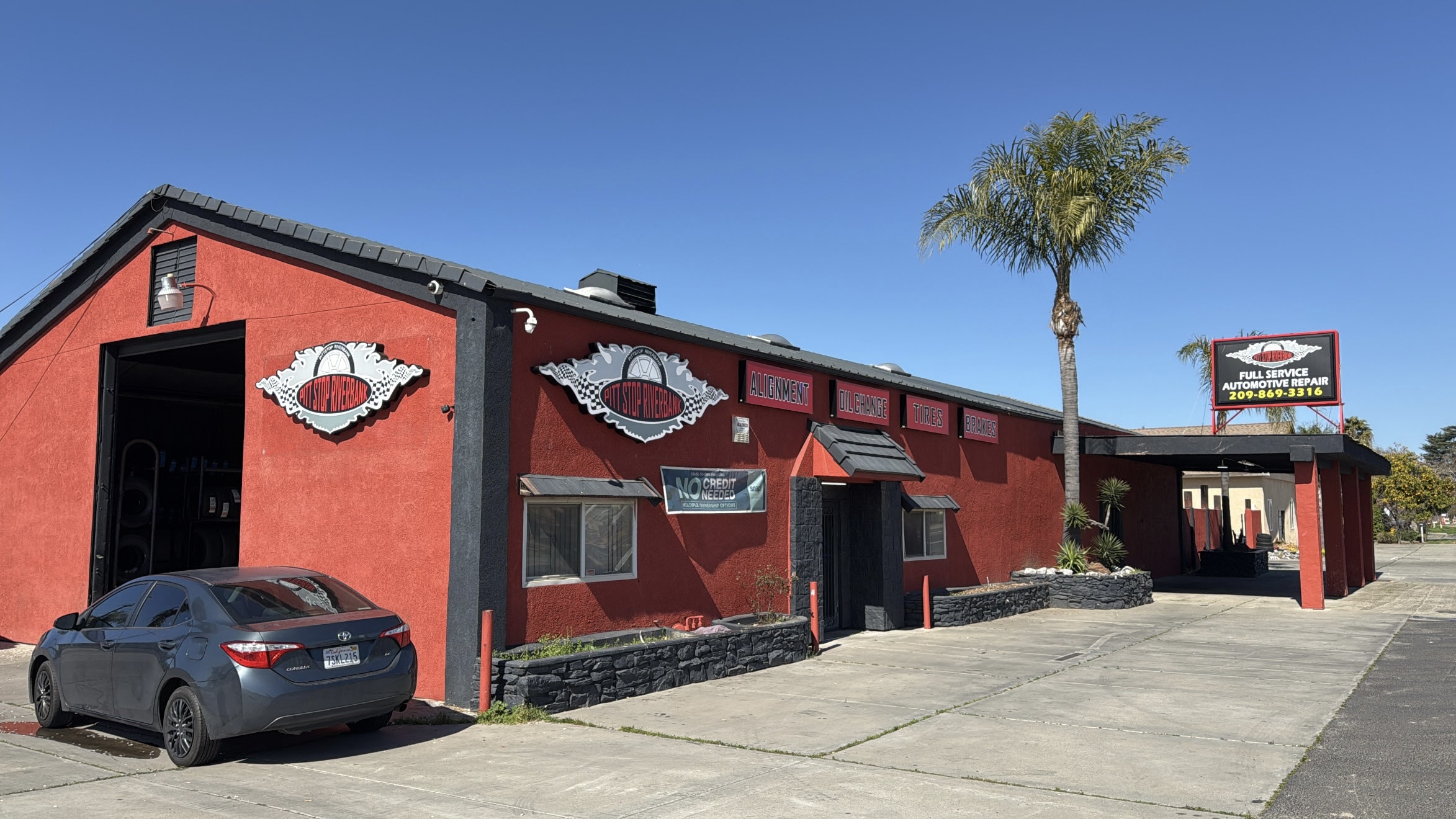 Auto repair shop with red building and palm tree.