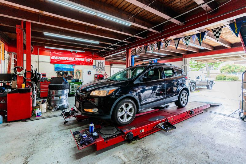 Auto repair shop with a black sedan on a hydraulic lift inside the workshop.