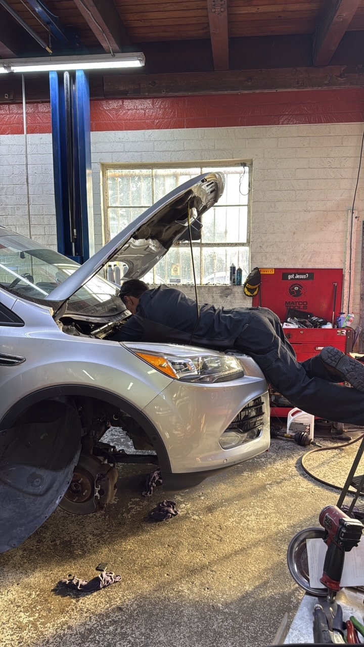 Auto mechanic inspecting engine under the hood of a silver car.