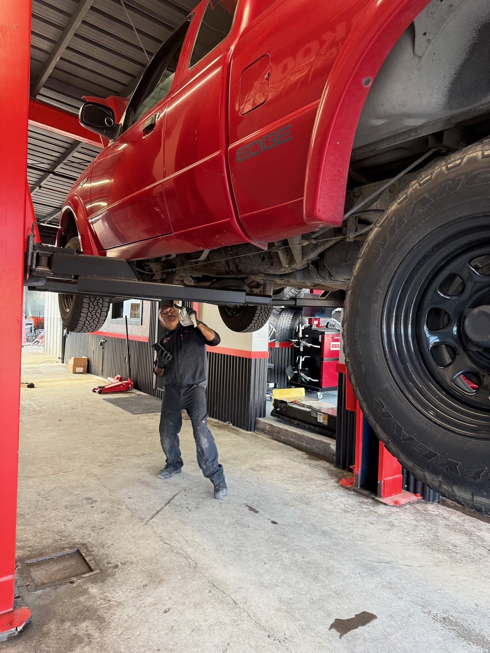 Red pickup truck elevated on hydraulic lift at Pittstop Auto Care.