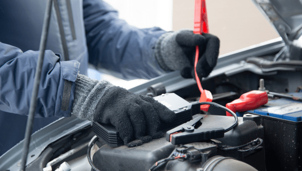 Jump-starting car battery with jumper cables for vehicle repair.