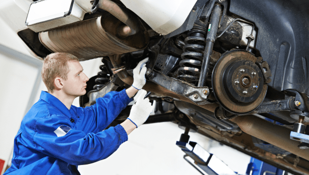 Skilled mechanic inspecting car suspension and undercarriage.