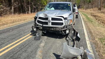 Damaged silver pickup truck after collision on rural road.