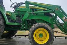 Green Johnnys Automotive tractor with front loader and yellow wheels.