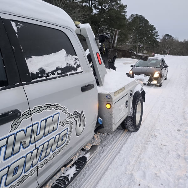 Emergency roadside towing service with snow-covered tow truck assisting stranded vehicle.