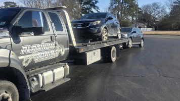 Heavy-duty tow truck transporting a black SUV and a silver car on a flatbed.