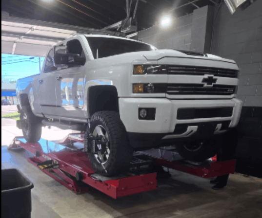 White Chevrolet Silverado truck on alignment lift at POPS FULL SERVICE.