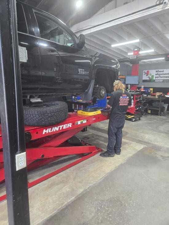 Auto repair technician working on a black truck in a service bay.