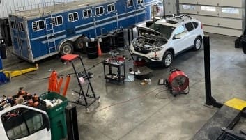 Auto repair technicians working on a white SUV engine.