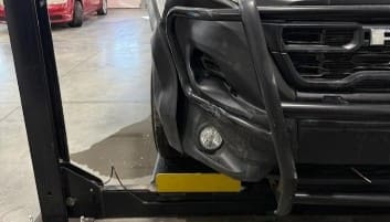 Auto repair technician inspecting a vehicle's front bumper and wheel area.