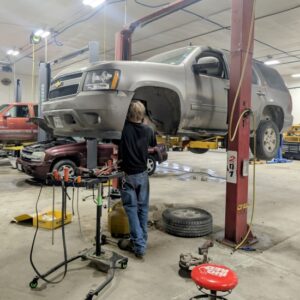 Auto repair shop with a lifted Chevrolet SUV undergoing maintenance or repair. Skilled technician wo.