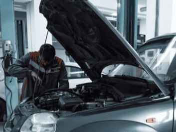 Auto repair technician inspecting engine under open hood.
