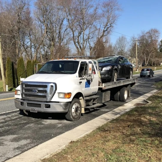 Tow truck transporting a black car on a suburban street.