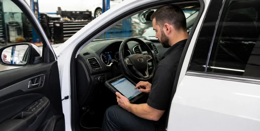 Auto technician using a tablet inside a vehicle at Qwik Oil & Auto Care.