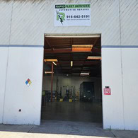 Commercial vehicle repair shop with open garage door and equipment inside.